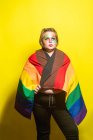 Modèle féminin en surpoids avec maquillage créatif montrant le drapeau LGBT et regardant loin sur fond jaune — Photo de stock