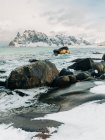 Acqua fredda del mare spruzzata sulle rocce vicino alla costa ghiacciata e innevata vicino alle montagne nella grigia giornata invernale sulle Isole Lofoten, Norvegia — Foto stock