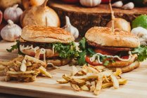 Antipasti hamburger con verdure e cotolette disposti su tavola di legno con patatine fritte in cucina — Foto stock