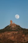 Paisaje espectacular con gran luna llena en el cielo azul sobre el pico rocoso de la montaña con bosque verde en la noche de verano - foto de stock