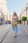 Mulher encantadora segurando um chapéu de palha olhando para longe no dia ensolarado na rua da cidade no verão — Fotografia de Stock