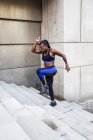Вид сбоку на сильную афроамериканку, бегущую по лестнице во время тренировки возле современного здания на городской улице — стоковое фото