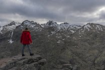Rückansicht eines nicht wiedererkennbaren Mannes in Oberbekleidung, der auf einem Stein steht und auf den schneebedeckten Gebirgskamm der Sierra de Gredos blickt, am bewölkten Abend in Avila, Spanien — Stockfoto