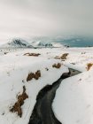 Узкий ручей с холодной водой, текущей под снегом против гор и облачного неба на Лофотенских островах, Норвегия — стоковое фото
