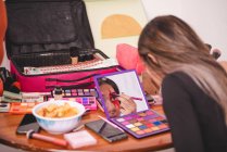 Giovane femmina guardando specchio e pittura ornamento sul viso mentre si applica trucco creativo in studio — Foto stock