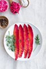 From above gravlax with mixed peppercorns and fresh dill sprigs on plate on light background — Stock Photo