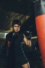 Jovem focado homem asiático treinamento boxe realizando socos durante o exercício com pesado saco de perfuração em um ginásio moderno — Fotografia de Stock