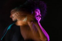 Приємний латиноамериканський чоловік у навушниках слухає музику і кудряче волосся у студії з неоновими вогнями на чорному фоні. — стокове фото