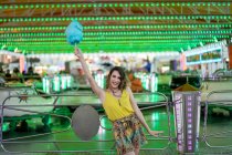 Mujer optimista de pie con algodón azul de azúcar en el brazo levantado mientras disfruta de fin de semana en el parque de atracciones y mirando a la cámara - foto de stock