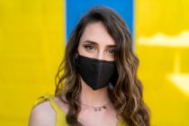 Content female with wavy hair wearing protective mask during coronavirus in city looking at camera on two colored background — Stock Photo