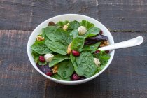 Haut angle de délicieuse salade aux épinards et haricots et noix servie dans un bol sur une table en bois pour un déjeuner sain — Photo de stock