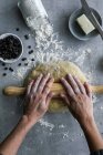 Mano de corte de hembra irreconocible utilizando herramienta de madera para rodar masa fresca para pastelería en cocina acogedora - foto de stock