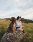 Proprietária feminina com cão Labradoodle obediente sentado na rocha nas montanhas — Fotografia de Stock