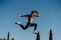 Вид збоку активного спортсмена-чоловіка в спортивному одязі, стрибки під час кардіо-тренувань на сонячному світлі — стокове фото