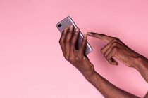 Recortar las manos de hombre afroamericano sosteniendo el teléfono y haciendo gesto aislado sobre fondo rosa - foto de stock