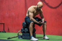 Seitenansicht eines erschöpften, muskulösen Mannes, der beim funktionellen Training im Fitnessstudio auf Gewichten sitzend wegschaut und sich ausruht — Stockfoto