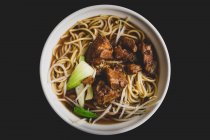 Крупный план миски восхитительного азиатского супа из лапши со свиными ребрышками на столе кафе — стоковое фото