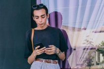 Baixo ângulo de gay masculino mensagens no social media no celular enquanto em pé no rua e sorrindo — Fotografia de Stock