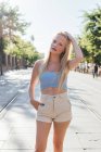 Charming female with blond hair and in trendy summer clothes standing with hand in pocket in city and looking at camera — Stock Photo