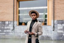 Портрет элегантного черного мужчины в сером пальто на улице, смотрящего в камеру — стоковое фото
