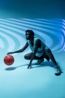 Черная женщина в баскетбольной форме в студии с помощью цветных гелей и проектора огней на синем фоне — стоковое фото
