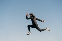 Vue latérale de l'athlète masculin actif en vêtements de sport sautant pendant l'entraînement cardio au soleil — Photo de stock