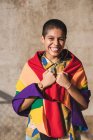 Вміст молодої бісексуальної етнічної жінки з різнокольоровим прапором, що представляє символи ЛГБТК, які дивляться на камеру в сонячний день — стокове фото