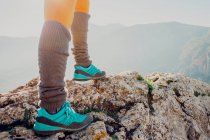 Невпізнаваний дослідник в похідних чоботях, що стоять на скелястому пагорбі в високогір'ї в сонячний день — стокове фото