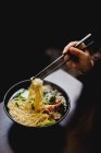 Hand of unrecognizable woman picking noodles with chopsticks from bowl of savory Asian soup in cafe — Stock Photo