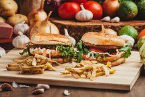 Appetitliche Hamburger mit Gemüse und Schnitzel auf Holzbrett mit Pommes in der Küche — Stockfoto
