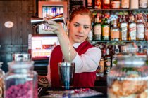 Konzentrierte Barkeeperin in Uniform gießt Alkohol aus Jigger in Shaker, während sie Cocktails in Bar zubereitet — Stockfoto