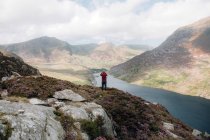 Vista posterior de hombres anónimos que admiran las colinas y el río mientras están de pie en una pendiente áspera durante el viaje a través de Snowdonia, Reino Unido - foto de stock