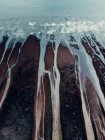 Сверху воздушный текстурированный ландшафт грубого неровного каменистого берега и пенные океанские волны с потоками — стоковое фото