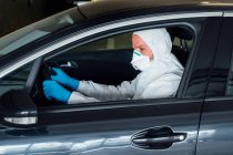Side view of serious biologist man using a protective mask, gloves and clothes while driving car during quarantine time — Stock Photo