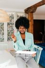 Moderna donna afro-americana freelance di successo in abito elegante con capelli afro seduta a tavola e documento di lettura a casa — Foto stock