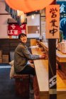 Femme asiatique en tenue décontractée assise au comptoir en bois en attendant l'ordre dans ramen bar — Photo de stock