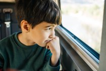 Vista lateral de un niño mirando por la ventana de una autocaravana - foto de stock
