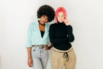 Cheerful young pink haired woman and African American girlfriend in stylish outfit standing together on white background — Stock Photo