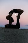 Vista laterale della silhouette della donna flessibile che fa backbend e bilanciamento sulle gambe dell'uomo durante la sessione di acroyoga contro il cielo del tramonto con la luna — Foto stock