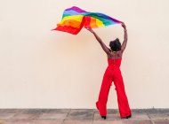 Stilvolle Afroamerikanerin in trendiger Kleidung mit bunter Fahne, die beim Feiern wegschaut — Stockfoto