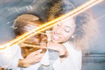 Cheerful young African American male giving piggyback ride to happy girlfriend with curly hair in trendy outfit near freeze lights — Stock Photo