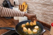 Crop anonyme ethnische Person braten Kochen Bananenstücke in Pfanne mit heißem Öl auf Herd, während die Zubereitung von Patacones in der Küche — Stockfoto