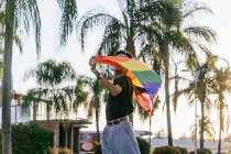 Entzückte männliche Homosexuelle stehen mit geschlossenen Augen und hissen während des Sonnenuntergangs in der Stadt die Regenbogen-LGBT-Flagge — Stockfoto