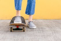Ausgeschnittene unkenntliche Skaterin mit Skateboard steht tagsüber auf Gehweg mit bunter gelber Wand auf dem Hintergrund — Stockfoto