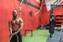 Сильний спортсмен тягне мотузку з важкими вагами під час інтенсивних тренувань у сучасному тренажерному залі — стокове фото