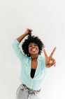 Jovem afro-americana brincalhão em roupa da moda se divertindo e mostrando língua e sinal de paz no fundo branco — Fotografia de Stock