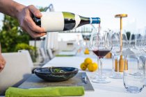 Camarero vertiendo vino tinto en una copa en el restaurante de alta cocina al aire libre - foto de stock