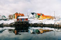 Снежная набережная в мирном прибрежном поселении с красными домами в пасмурный зимний день на Лофских островах, Норвегия — стоковое фото