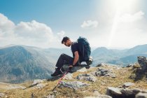 Vista lateral del hombre viajero sentado descansando durante el senderismo en las montañas con bastón de trekking durante las vacaciones en verano en Gales - foto de stock