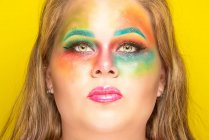 Além de tamanho feminino com maquiagem colorida brilhante olhando para a câmera contra fundo amarelo — Fotografia de Stock